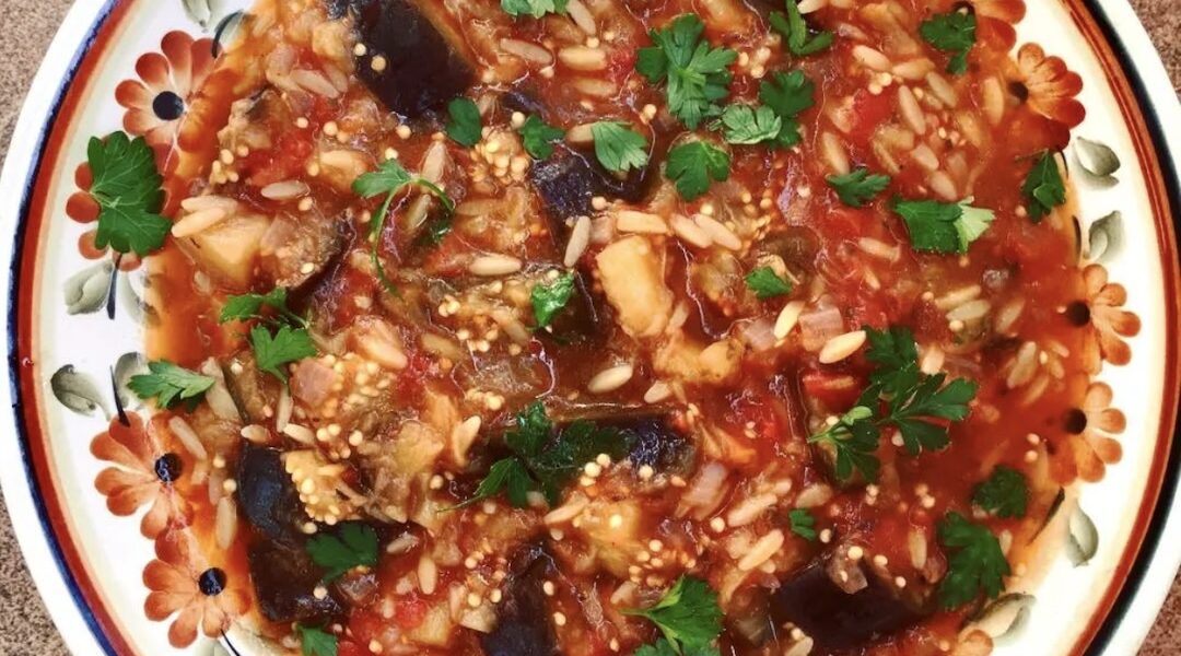 Drobno krojony bakłażan duszony razem z cebulą, pomidorami i świeżymi ziołami z dodatkiem makaronu kritharaki.