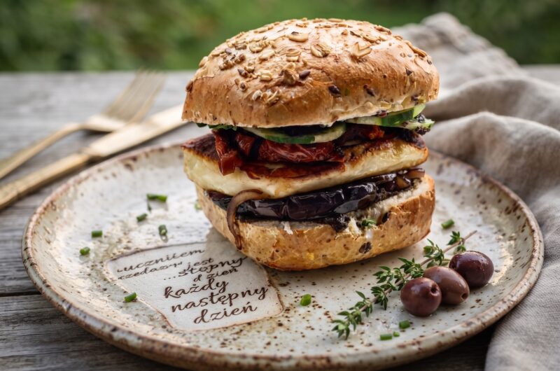 Burger wegetariański przygotowany na bazie tapenady z grillowanym serem halloumi, plastrami bakłażana, karmelizowaną cebulą a także z chrupiącymi warzywami.