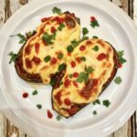 Przekrojony wzdłuż na połowę bakłażan pieczony, a następnie wypełniony aromatycznym duszonym mięsem i zapiekany pod pierzynką beszamelu.