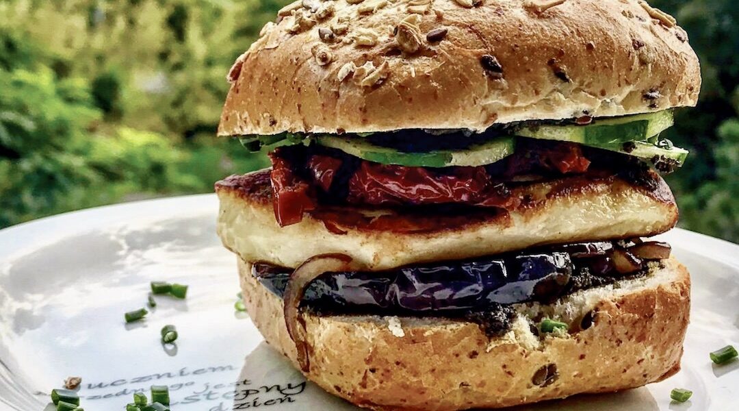 Burger wegetariański przygotowany na bazie tapenady z grillowanym serem halloumi, plastrami bakłażana, karmelizowaną cebulą a także z chrupiącymi warzywami.