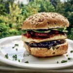 Burger wegetariański przygotowany na bazie tapenady z grillowanym serem halloumi, plastrami bakłażana, karmelizowaną cebulą a także z chrupiącymi warzywami.