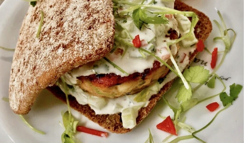 Burger z mielonego mięsa łososia i surowych krewetek doprawiony po azjatycku podany z dipem kolendrowym w świeżej bułce.