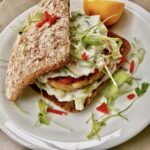 Burger z mielonego mięsa łososia i surowych krewetek doprawiony po azjatycku podany z dipem kolendrowym w świeżej bułce.