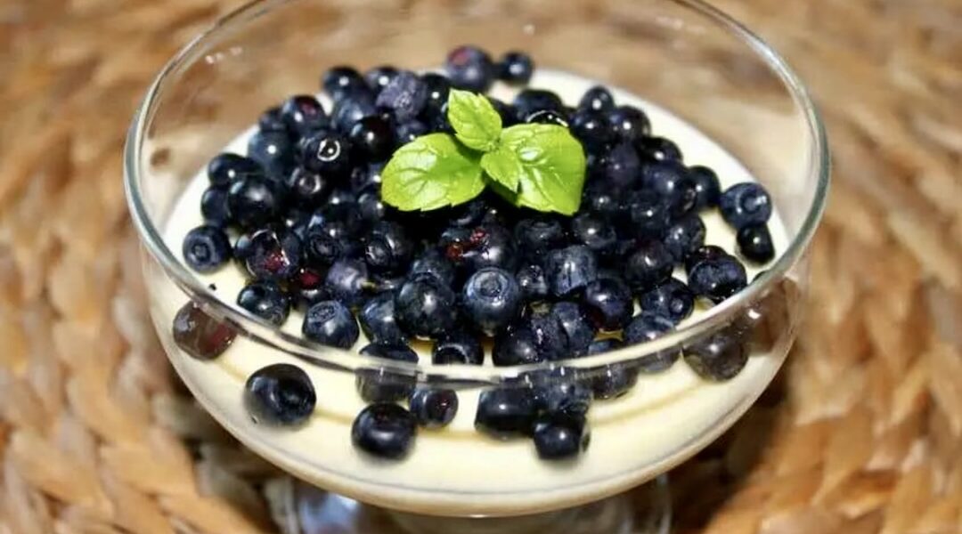 Deser cytrynowy zrobiony ze słodkiej śmietanki z dodatkiem cukru i soku z cytryny po stężeniu posypany borówkami.