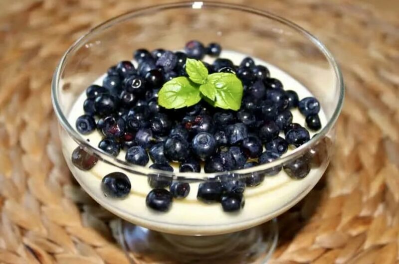 Deser cytrynowy zrobiony ze słodkiej śmietanki z dodatkiem cukru i soku z cytryny po stężeniu posypany borówkami.