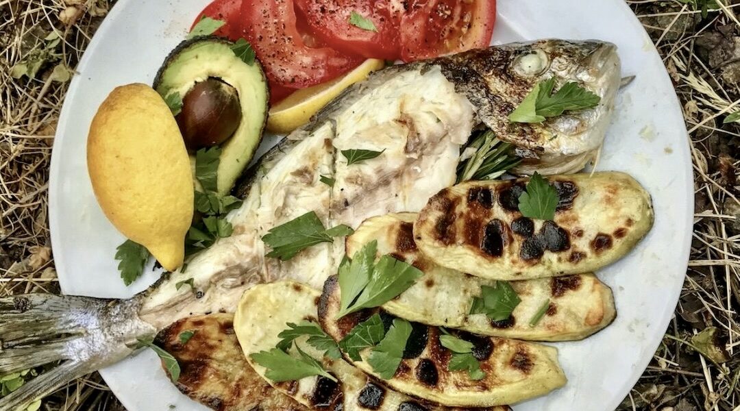 Dorada z grilla to ryba marynowana najpierw w oliwie z dodatkiem czosnku, a następnie wypełniona plastrami cytryny i świeżym rozmarynem i pieczona rna uszcie.