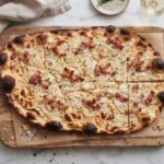 Flammkuchen alzacki to prosty podpłomyk przygotowany z mąki i wody. Na cieniutko rozwałkowane ciasto nakłada się śmietanę, a następnie piórka cebuli i plasterki wędzonego boczku. Pieczemy bardzo krótko w bardzo wysokiej temperaturze.