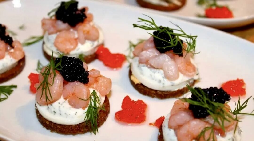 Małe szwedzkie kanapki z ciemnego pieczywa obłożone plastrami gotowanego jajka z sosem koperkowym oraz krewetkami koktajlowymi i kawiorem.