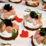 Małe szwedzkie kanapki z ciemnego pieczywa obłożone plastrami gotowanego jajka z sosem koperkowym oraz krewetkami koktajlowymi i kawiorem.