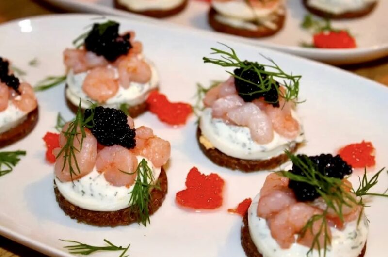 Małe szwedzkie kanapki z ciemnego pieczywa obłożone plastrami gotowanego jajka z sosem koperkowym oraz krewetkami koktajlowymi i kawiorem.