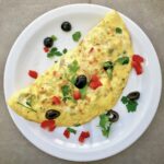 Omlet z łososiem wędzonym z dodatkiem oliwek, czerwonej papryki i startego parmezanu.