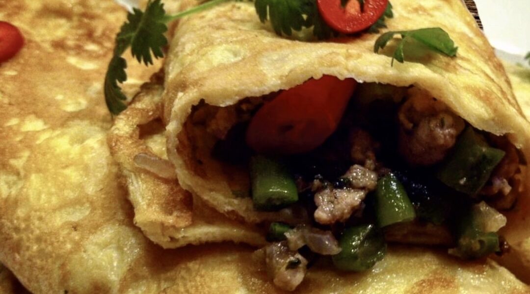 Omlet z wieprzowiną po tajsku to mielone mięso smażone razem z aromatyczną pastą z dodatkiem fasolki szparagowej, a następnie zawinięte w prosty omlet usmażony z rozkłóconych jajek