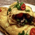 Omlet z wieprzowiną po tajsku to mielone mięso smażone razem z aromatyczną pastą z dodatkiem fasolki szparagowej, a następnie zawinięte w prosty omlet usmażony z rozkłóconych jajek