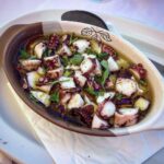 Ośmiornica gotowana w sosie własnym, a następnie krojona i zalana sosem winegret z dodatkiem kawałków świeżej papryki i natki pietruszki.