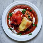 Papryka faszerowana kurczakiem to przekrojone na połowę papryki wypełnione farszem z kurczaka i ryżu, a następnie zapiekane i podane na sosie pomidorowym.