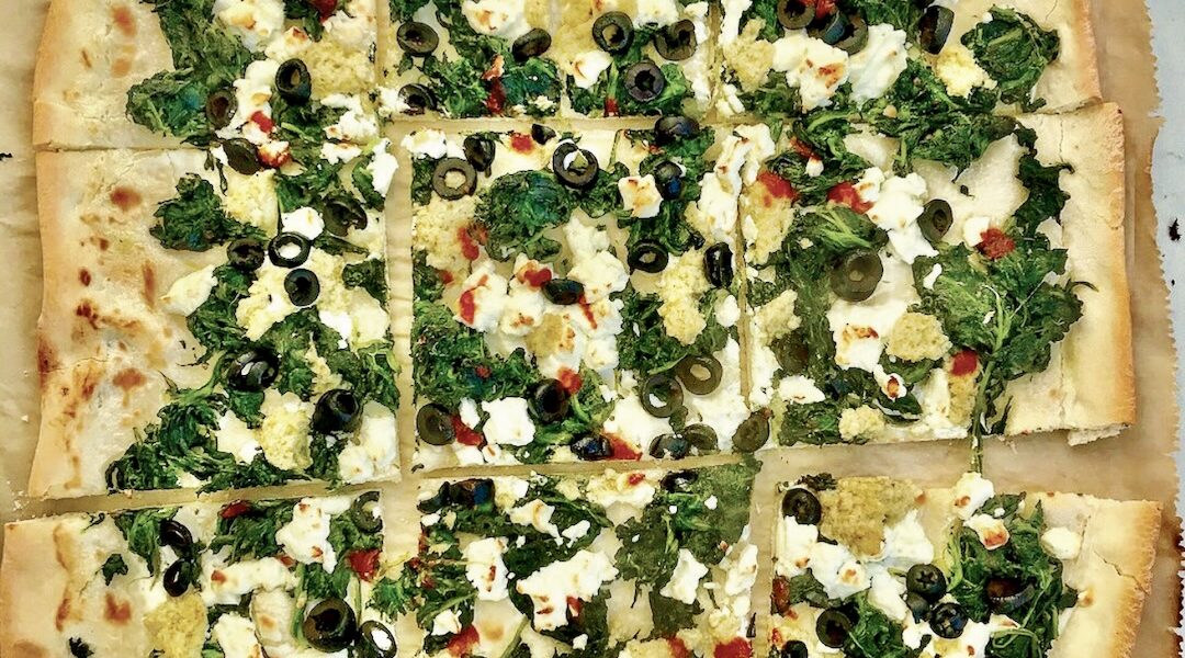 Podpłomyk ze szpinakiem i fetą to proste ciasto z mąki i wody rozwałkowane na cienki placek, a następnie obłożony duszonym szpinakiem, serem feta i oliwkami i krótko pieczony.