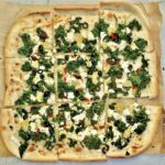 Podpłomyk ze szpinakiem i fetą to proste ciasto z mąki i wody rozwałkowane na cienki placek, a następnie obłożony duszonym szpinakiem, serem feta i oliwkami i krótko pieczony.