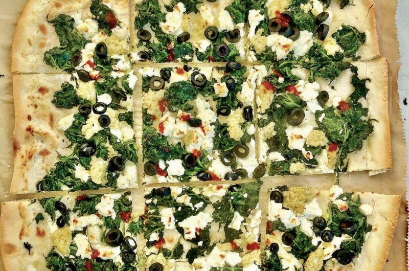 Podpłomyk ze szpinakiem i fetą to proste ciasto z mąki i wody rozwałkowane na cienki placek, a następnie obłożony duszonym szpinakiem, serem feta i oliwkami i krótko pieczony.