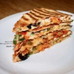 Quesadilla z pieczarkami to tortilla obłożona wędliną, startym serem, papryką i szparagami, następnie przykryta drugą tortillą i podgrzana na patelni.