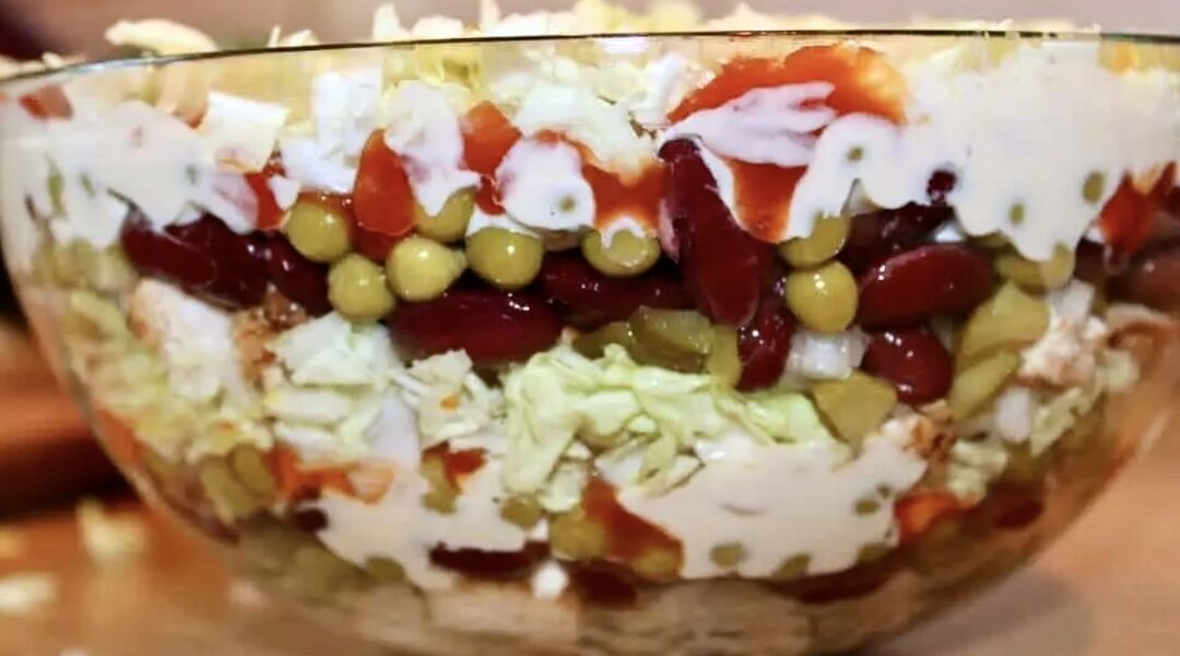 Sałatka warstwowa z kurczakiem przyrządzona została ze smażonej w przyprawach piersi z kurczaka, która po pokrojeniu ułożona została naprzemiennie z groszkiem, czerwoną fasolką, siekanymi ogórkami kiszonymi, a także kapustą pekińską. Całą sałatkę spoił majonez.