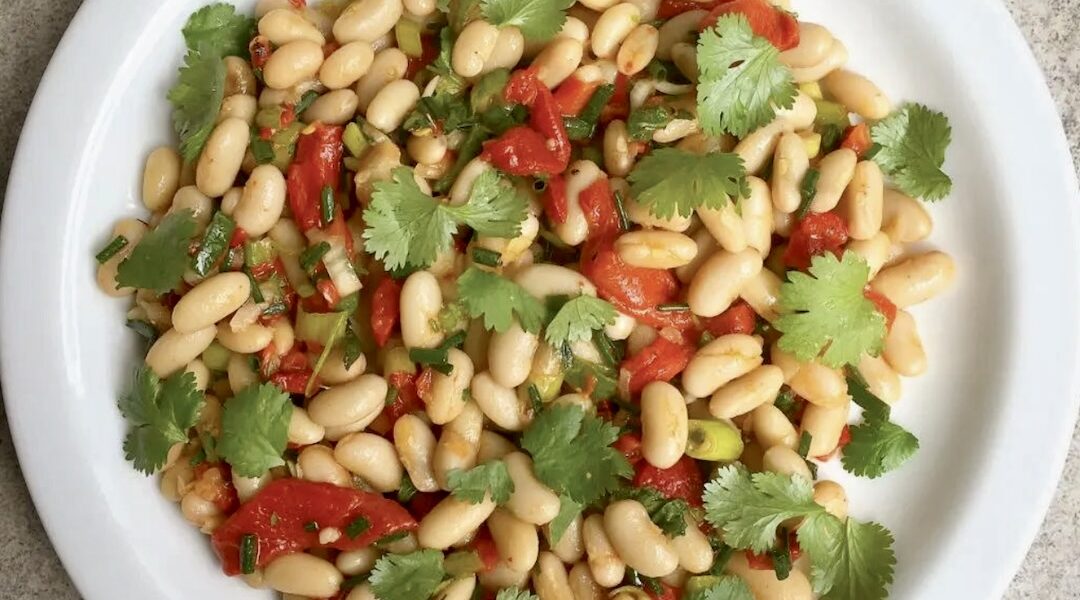 Sałatka z białej fasolki z puszki z dodatkiem marynowanej czerwonej papryki, świeżej kolendry i dymki skropiona oliwą i sokiem z cytryny.
