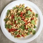 Sałatka z białej fasolki z puszki z dodatkiem marynowanej czerwonej papryki, świeżej kolendry i dymki skropiona oliwą i sokiem z cytryny.