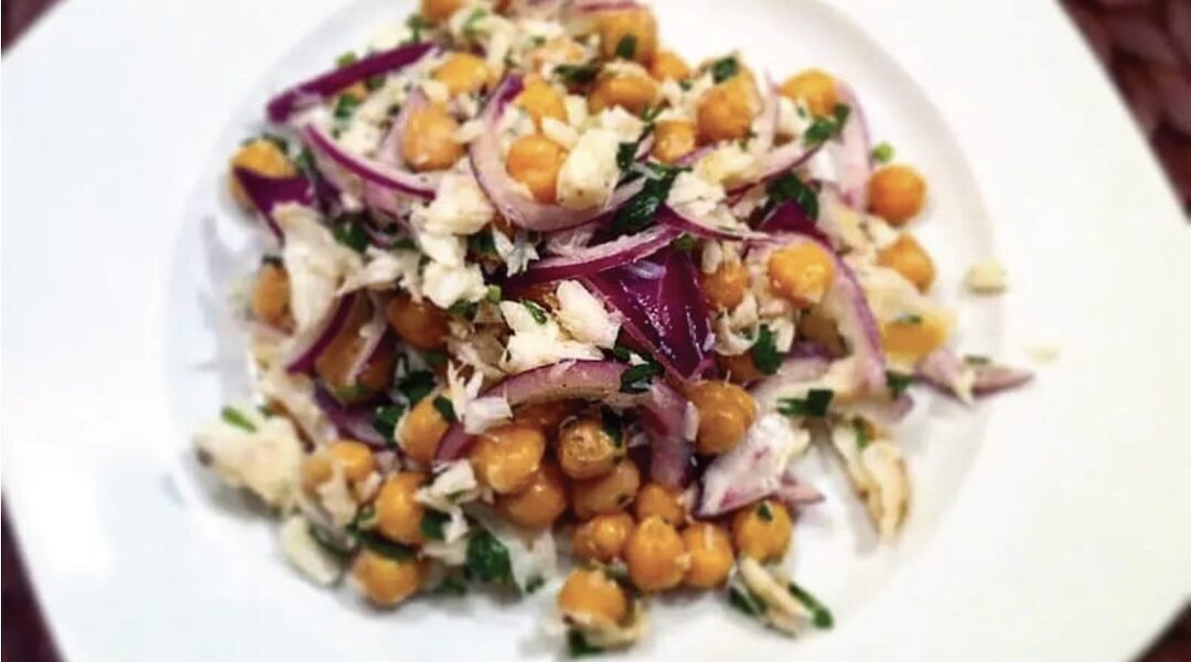 Sałatka z ciecierzycy z puszki z dodatkiem czerwonej cebuli i wędzonego dorsza skropiona oliwą extra vergine.