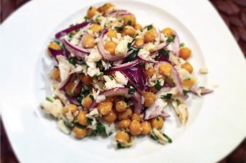 Sałatka z ciecierzycy z puszki z dodatkiem czerwonej cebuli i wędzonego dorsza skropiona oliwą extra vergine.