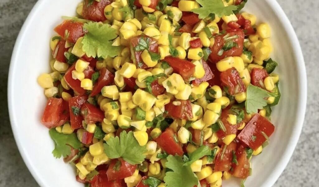 Sałatka z kukurydzą może być świetnym dodatkiem do niemal każdego posiłki. Przygotowana została ziaren kukurydzy gotowanej, posiekanych pomidorów, ostrych papryczek, dymki i świeżej kolendry, a przed podaniem skropiona sokiem z limonki i oliwą.