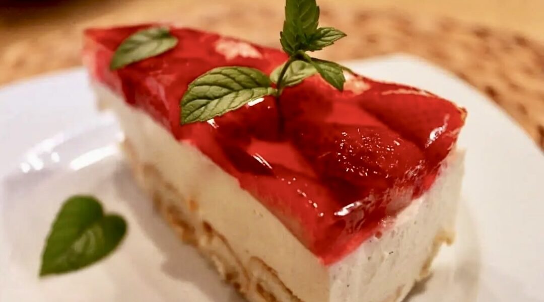Sernik na zimno na spodzie z biszkoptów pokrytych masą z jajek, cukru i twarogu pokrytej galaretką i ozdobioną truskawkami.