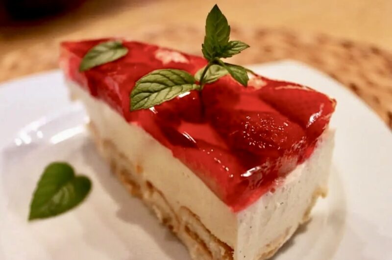Sernik na zimno na spodzie z biszkoptów pokrytych masą z jajek, cukru i twarogu pokrytej galaretką i ozdobioną truskawkami.