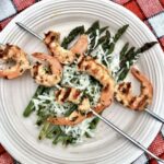 Szaszłyki z krewetek przygotowuję zawsze z surowych krewetek, które uprzednio marynuję w oliwie z dodatkiem czosnku. Tak przygotowane szaszłyki wystarczy bardzo krótko piec na ruszcie, by poczuć ich pełny aromat.