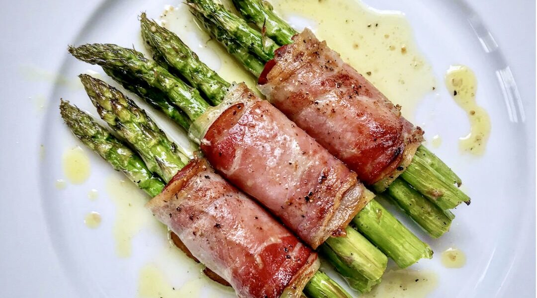 Zielone szparagi owinięte plastrami szynki dojrzewającej, pieczone i skropione oliwą extra vergine tuż przed podaniem.