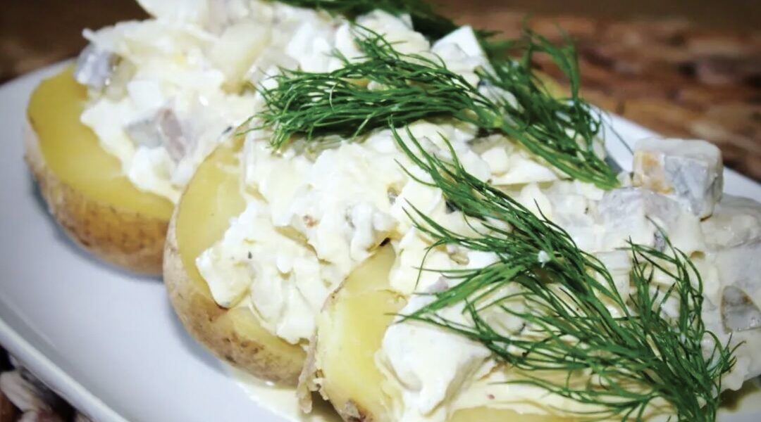 Gotowane ziemniaki podane z sałatką śledziową ze śledzia matiasa, ogórków kiszonych, jajka gotowanego i kwaśnej śmietany.