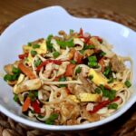 Bami Goreng to makaron wymieszany ze smażonymi kawałkami kurczaka, cebulą oraz warzywami, szynką i siekanym omletem.