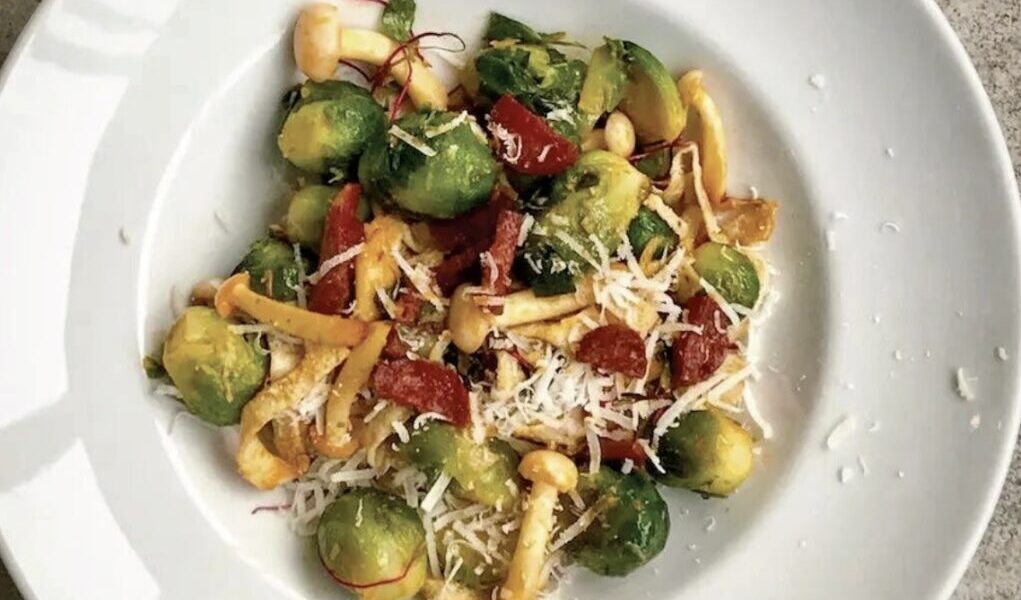 Gotowana brukselka smażona z plastrami chorizo i grzybami shimeji na koniec posypana parmezanem.