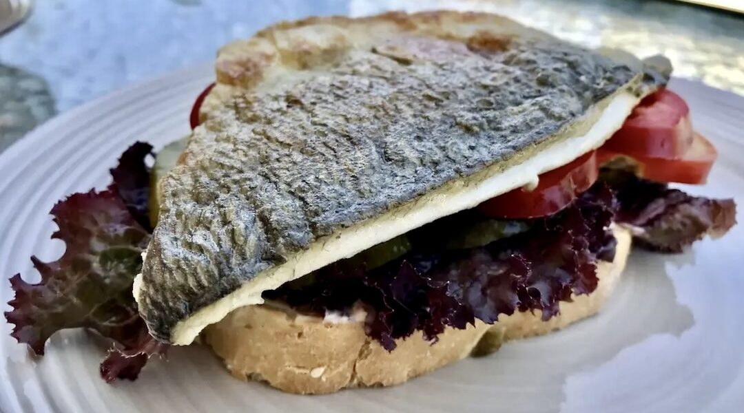 Burger z doradą smażoną w formie fileta wypełniony kawałkami awokado i plastrami pomidora.