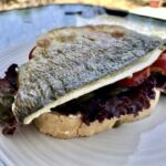 Burger z doradą smażoną w formie fileta wypełniony kawałkami awokado i plastrami pomidora.