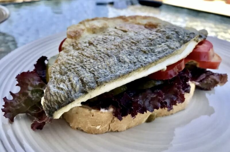 Burger z doradą smażoną w formie fileta wypełniony kawałkami awokado i plastrami pomidora.