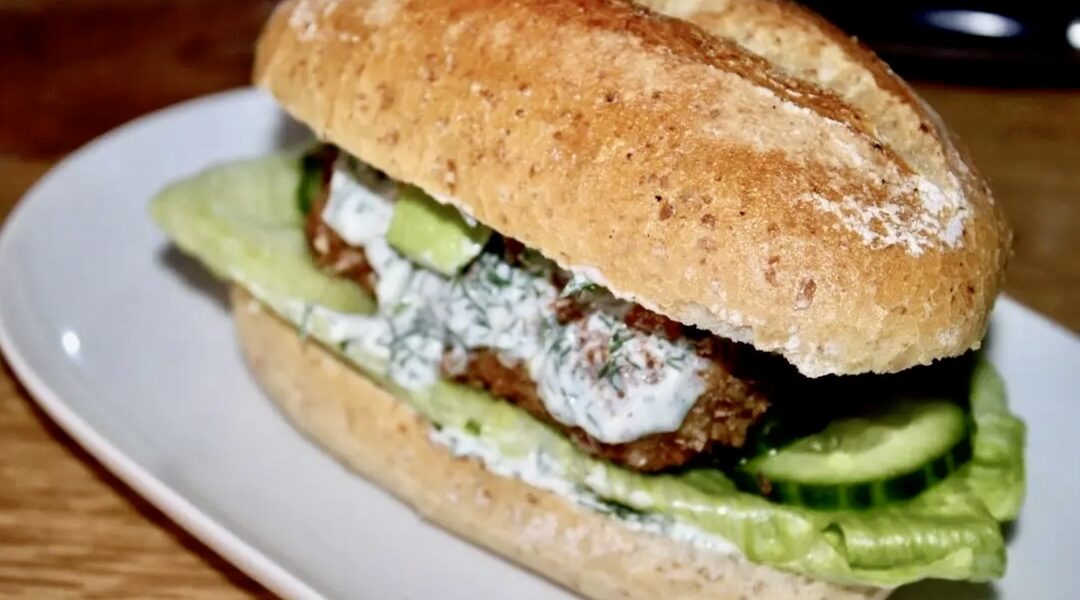 Burger z dorszem smażonym w panierce podany w bułce z dodatkiem awokado i chilli oraz z sosem koperkowym.