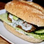 Burger z dorszem smażonym w panierce podany w bułce z dodatkiem awokado i chilli oraz z sosem koperkowym.