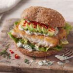 Burger z dorszem smażonym w panierce podany w bułce z dodatkiem awokado i chilli oraz z sosem koperkowym.