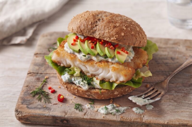 Burger z dorszem smażonym w panierce podany w bułce z dodatkiem awokado i chilli oraz z sosem koperkowym.