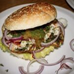 Pyszny burger ze śledziem smażonym podanym w bułce razem z dodatkiem sałatki Coleslaw, ogórkiem kiszonym i czerwoną cebulą.