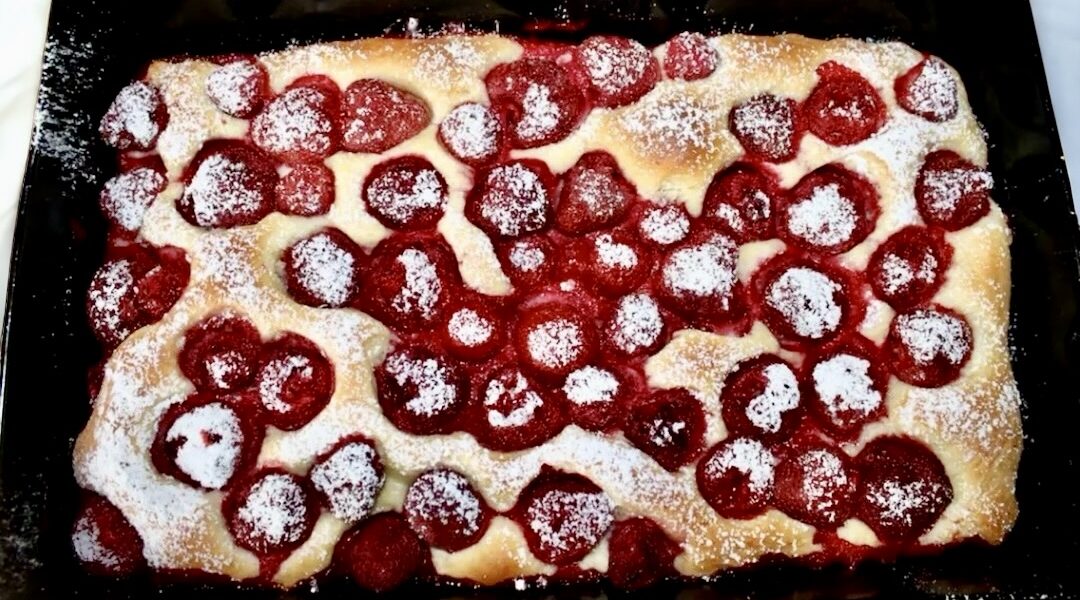Puszyste ciasto drożdżowe z dojrzałymi słodkimi truskawkami posypane po upieczeniu cukrem pudrem.