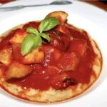 Cukinia pokrojona w kostkę i duszona z czosnkiem w pomidorach podawana z polentą z grzybami.