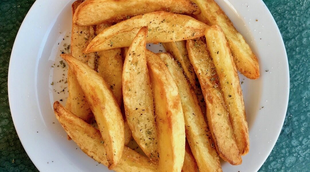 Frytki greckie to wykrojone z dużych podłużnych ziemniaków ósemki smażone w oliwie i na koniec sypane solą morską i oregano.