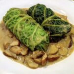 Gołąbki wegetariańskie to liście kapusty włoskiej wypełnione farszem ze świeżych i mielonych grzybów z dodatkiem kaszy jaglanej, zawinięte, duszone i podane w sosie grzybowym.