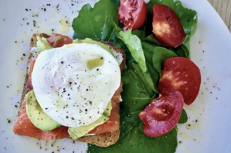 Kanapka z łososiem wędzonym na zimno przygotowana z chleba tostowego posmarowanego serkiem obłożona dodatkowo awokado i jajkiem w koszulce.