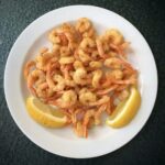 Małe krewetki koktajlowe obsypane mąką, a następnie smażone w oliwie i podane z cytryną.